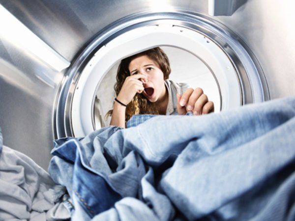 Девушка, затыкающая нос, заглядывая в стиральную машину