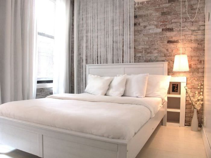 Белая кровать в спальне с кирпичной стеной